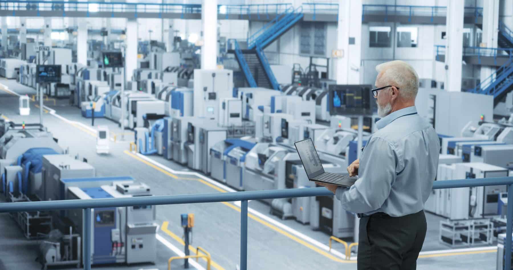 A manufacturing technician reviewing a laptop on a walkway above an electronics production line